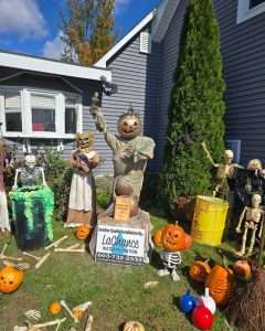 Lakes Region Water Filtration & Treatment 8 Pumpkin-head Statue of Liberty figure next to a LaChance Water Filtration sign, surrounded by jack-o-lanterns and skeletons
